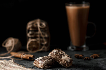 Two gingerbread cookies are on the table. In the background, a large glass with a brown drink. Without man. Artistic effect of a blurred background.