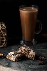 Two gingerbread cookies are on the table. In the background, a large glass with a brown drink. Without man. Artistic effect of a blurred background.
