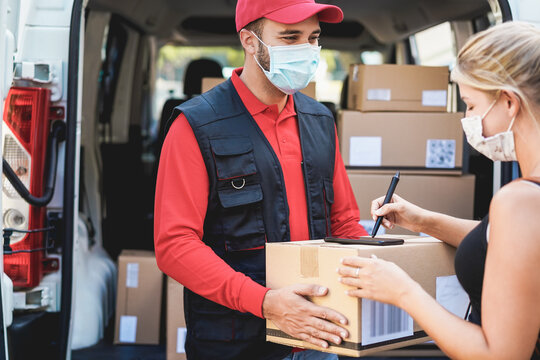 Young woman receiving a cardboard package from delivery man wearing face mask - Courier at work during coronavirus outbreak - Focus on right girl's hand