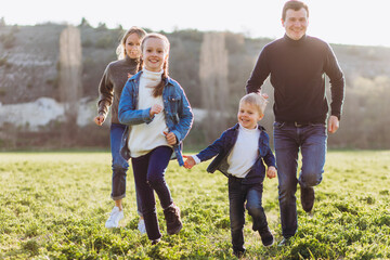 Father, mother and children run through a green field.