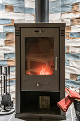 Modern wood burning stove with accessories and red gloves next to it. Wood burning stove with...