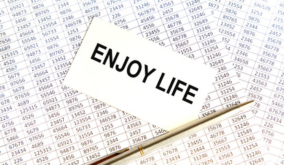 Obraz premium On the business card the text OF ENJOY LIFE, next to the pen. The background consists of reports. A business concept.