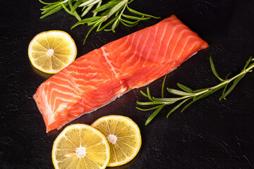 Lightly salted trout. Fresh fish fillet with culinary ingredients, herbs and lemon on a black background, side view.