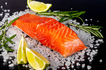 Lightly salted trout. Fresh fish fillet with culinary ingredients, herbs and lemon on a black background, side view.