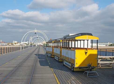 southport, merseyside, united kingdom - 28 june 2019: the yellow train on the pier in southport merseyside on a bright summer day with town buildings against a blue cloudy sky