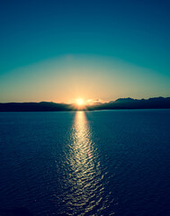 Calm sea sunrise - dark blue sky, warm sun and mountains in the foreground