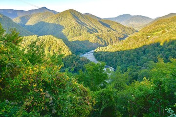 Mountain ranges in the evening with shadows on the slopes, covered with forest, with a river...