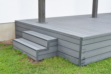 Part of dark gray or anthracite wpc composite meterial terrace deck with stairs  in backyard green grass outdoors.
