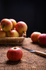 Ripe apples on burlap and in a basket on a black background. Back lighting. Rustic style, close-up.