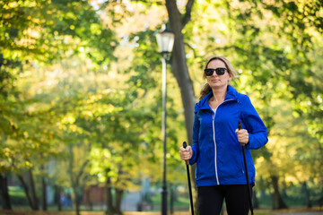 Nordic walking - middle-age woman training in city park
