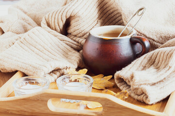 Cozy autumn composition with cup of herbal tea, warm woolen sweater, candles and bright oak leaves....