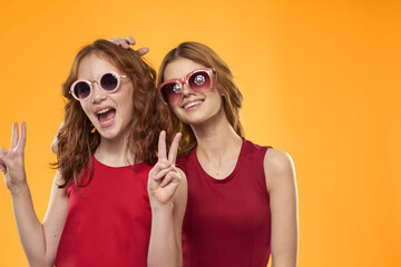 Happy sisters in red dresses on a yellow background are having fun and gesticulating Copy Space