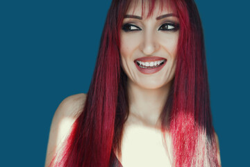 Fototapeta premium Portrait of happy charming red haired young woman wears looks to the camera, thinks and plans her birthday party isolated over blue background.evening make-up