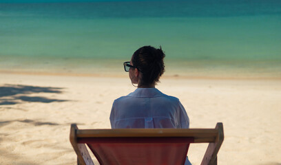 a back shot of woman from behind, she seats on sun chair and looks to the sea