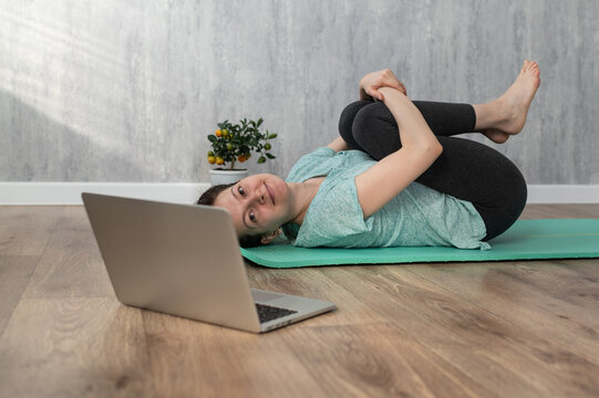 Young caucasian woman doing yoga exercise online. Knees to breast exercise