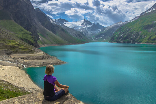 Girl sitting on rock and enjoying beautiful view of high mountain lake near Kaprun.Quiet relaxation in nature.Wonderful nature landscape,turquoise water,holiday travel scene.Wanderlust background