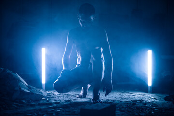 Handsome and strong man portrait posing with light of neon lamps and smoke over dramatic blue neon background in a dark room.  © deliris