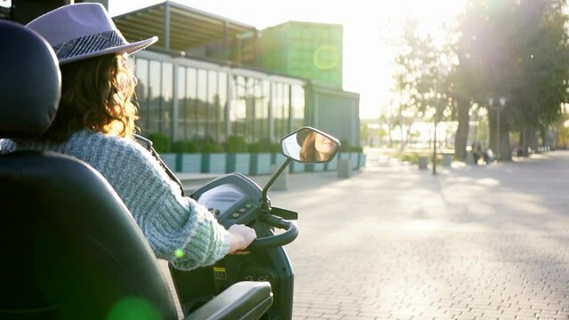 Woman tourist on a four wheel mobility electric scooter on a city street. Camera moves behind her, the woman's face is visible in the rearview mirror