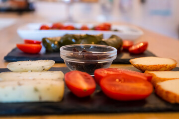 Different kinds of delicious and tasty cheese, with cherry tomatoes and isolated black greek olives. More food like italian bruschetta and hummus in background