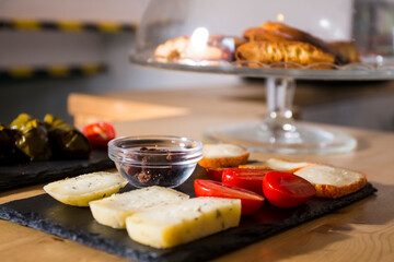 Different kinds of delicious and tasty cheese, with cherry tomatoes and isolated black greek olives. More food like italian bruschetta and hummus in background