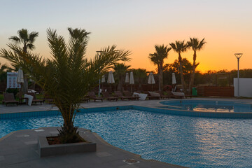 Swimming pool with sun loungers and umbrellas at sunset