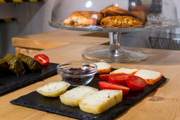 Different kinds of delicious and tasty cheese, with cherry tomatoes and isolated black greek olives. More food like olive oil stuffed leaves, cookies in background