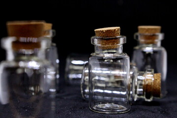 A close up photograph of small empty glass bottles with cork tops, against a black background