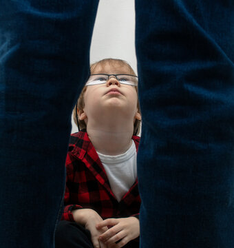 A little boy with glasses is sitting and looking up at the standing man in dismay. Domestic violence, kidnapping and child abuse concept