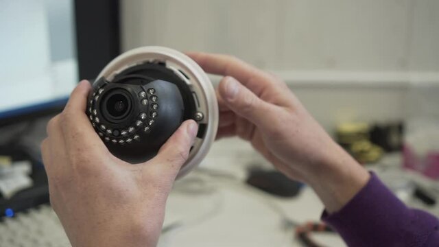 The Technician Repairman Adjusts the CCTV Camera for the Computer. Frame with Male Hands Holding the Camera, the background is Blurred. Setting up the CCTV Camera.