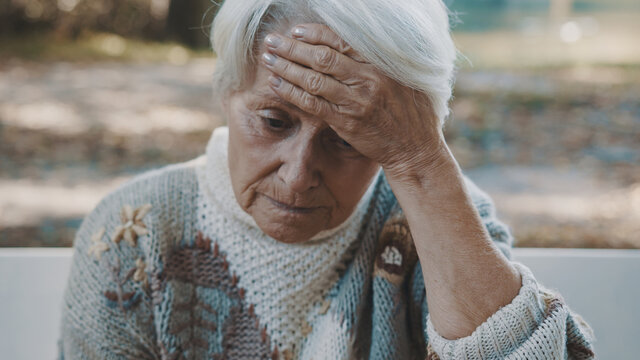 Portrait of elderly worried woman holding hand over her forehead in the park. High quality photo