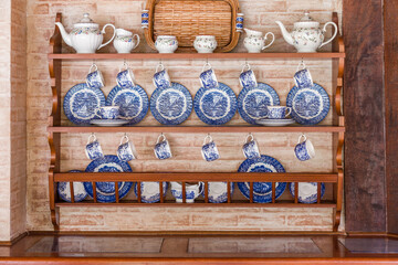 Set of white and blue dishes well organized in a wooden furniture in a brick back wall
