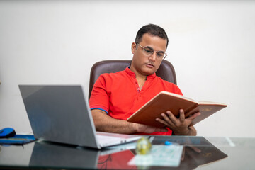technology, remote job and lifestyle concept - happy indian man in glasses with laptop computer working at office.