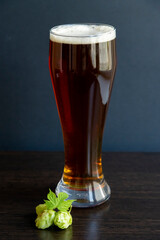 Close up view of drinking glass full of bear standing on wooden table by green hops crop. Food and drinks background. The theme of using natural ingredients.