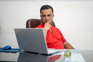 technology, remote job and lifestyle concept - happy indian man in glasses with laptop computer working at office.
