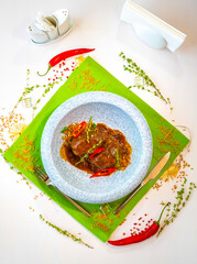 Stewed beef cheeks with spelled in a marble gray plate on a green tablecloth. Decor. Top view. Selective focus. Super short focus