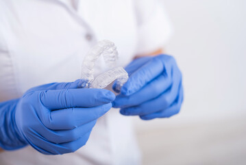 A faceless female orthodontist holds two transparent aligners. The dentist demonstrates the bite correction device