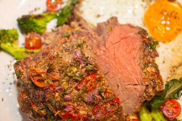 Roasted and seasoned meat with accompaniment of fried egg, brocolis, onion and tomato.