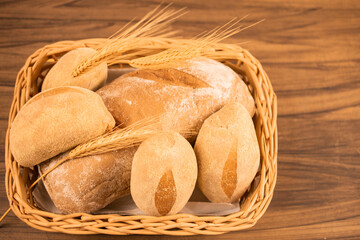 Australian and wholemeal bread in wicker basket on wooden background, with space for writing.Decorated with ear of wheat.