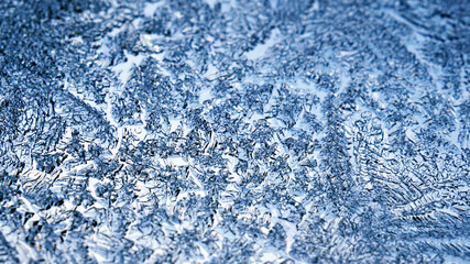 Ice crystals close-up on a window glass in winter. Frozen water. Cool fabulous abstract pattern. Blue and white background or wallpaper for Christmas and New Year. Strong macro