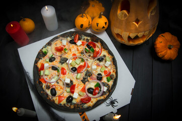Vegetable pizza on delivery box near Halloween decoration. Scary pumpkins with painted faces, Lights of burning candles In horror smoke. Dark background with cobwebs and spiders near fast food dish

