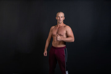 Fototapeta premium Pumped guy raises his thumb and smiles on a black background