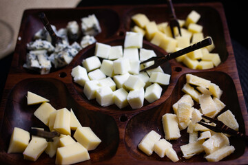 Wooden cheese board with gouda cheeses, fresh parmesan, parmesan and gorgonzola,  on a black topped table.