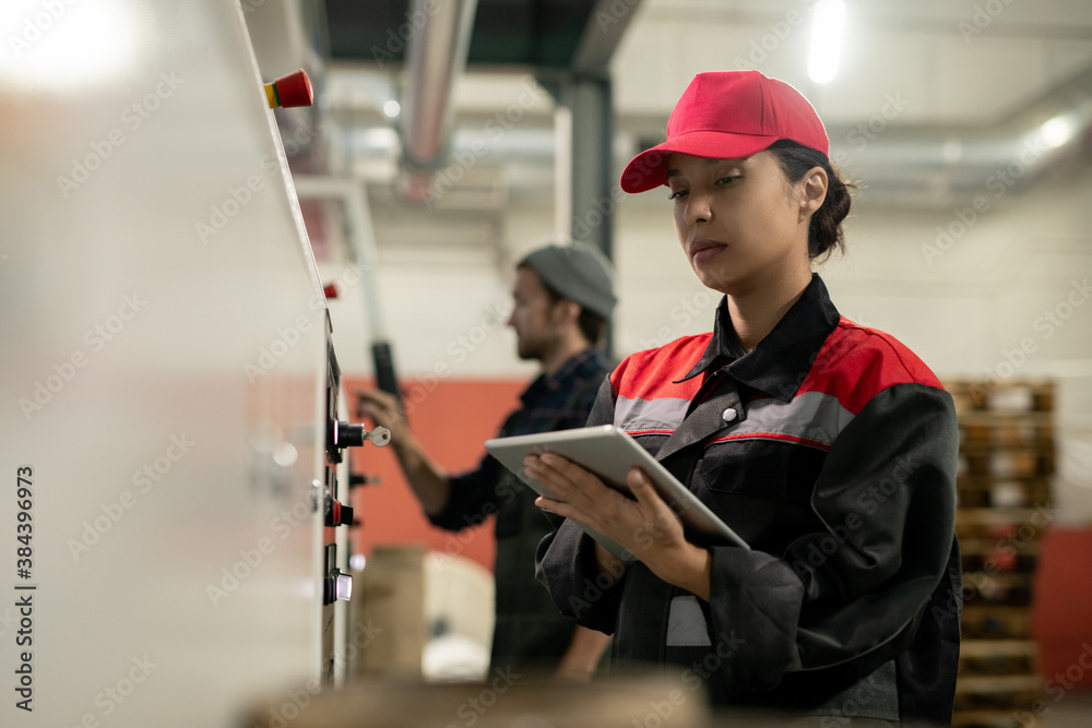 Poster young pretty female engineer with tablet entering data from control panel