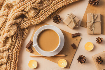 Cozy home flat lay: white cup with coffee, chunky knit scarf, notebook with pencil, gifts. The concept of the coming winter, christmas eve and new year. Warm shades, close-up.