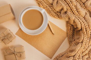Cozy home still life: a white cup with coffee, a chunky knit scarf, a notebook with a pencil. The concept of the coming winter, christmas eve and new year. Warm shades, close-up..