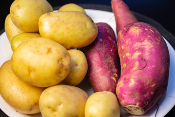 English potato and purple sweet potato in a white plate on a black table.