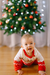 Baby girl in a Christmas-themed costume is crawling in front of a Christmas tree