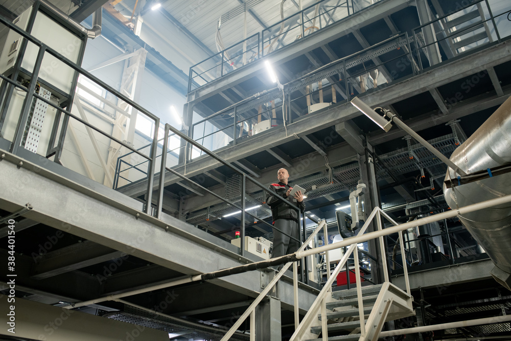 Poster Bald mature foreman with touchpad working inside polymer processing factory