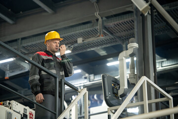 Confident mature foreman with hardhat on head and walkie talkie by his mouth