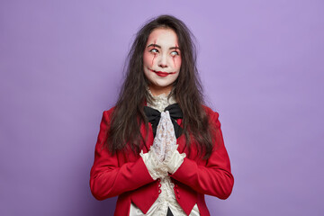 Horrible female zombie with bloody scars wears halloween festive makeup keeps palms pressed...